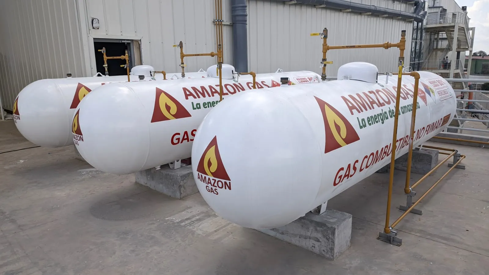 Tres tanques estacionarios blancos de Amazon Gas instalados junto a una nave industrial